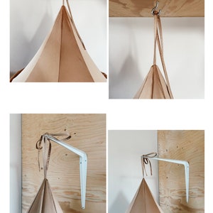May include: Two methods for hanging a tent-like structure. The first image shows a ceiling hook with a brown strap attached to it. The second image shows a white wall bracket with a brown strap attached to it. Both images show a brown tent-like structure.
