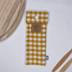 May include: A yellow and white gingham fabric pouch with a white button closure. The pouch is labeled "Pochette brosse a dent".