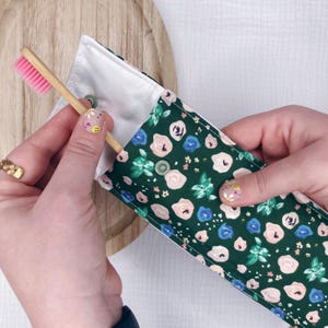 May include: A green floral fabric toothbrush holder with a white lining and a bamboo toothbrush with pink bristles.