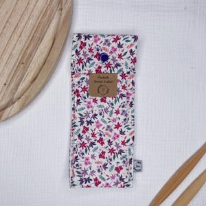 May include: A white fabric pouch with a floral print in shades of pink, purple, and green. The pouch has a button closure and a small label that reads "Pochette brosse a dent".