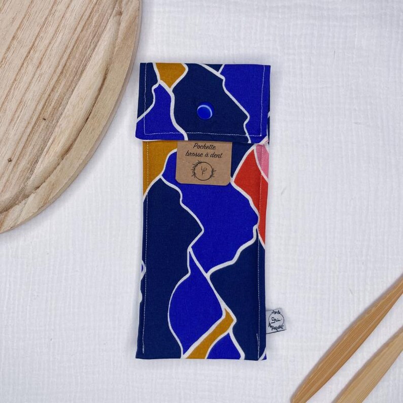 May include: A blue, orange, and red patterned fabric pouch with a snap closure. The pouch has a label that reads "Pochette brosse a dent".