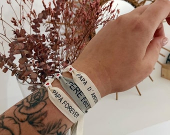 Op de afbeelding: Drie stoffen armbanden met de woorden "Papa d'Amour", "Pere  fect" en "Papa Forever" in zwarte tekst. Elk armband heeft een klein rood hart.