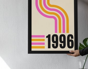 May include: A framed print with a retro design featuring curved orange and pink stripes on a cream background. The year 1996 is printed in black at the bottom of the print.