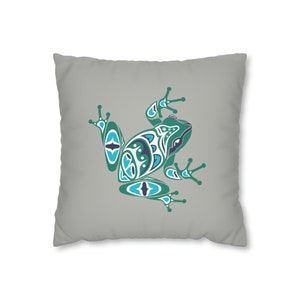 May include: A grey throw pillow featuring a green and blue stylised frog design. The frog is facing right and has a geometric pattern.