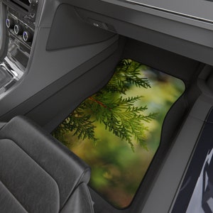 May include: A green and brown car floor mat with a close-up image of a cedar tree branch.
