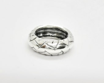 May include: A silver ring with a textured, woven design. The ring is thick and has a wide band.