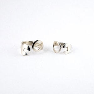 May include: Two silver rings with a unique design. The rings are open and have a curved shape.
