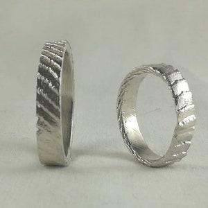 May include: Two silver rings with a textured, grooved design. The rings are side by side on a white surface.