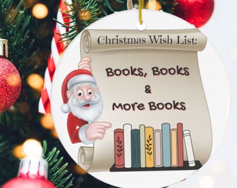 May include: A white ceramic Christmas ornament with a cartoon Santa Claus holding a scroll that reads "Christmas Wish List: Books, Books & More Books". The scroll is decorated with a bookshelf with colorful books.