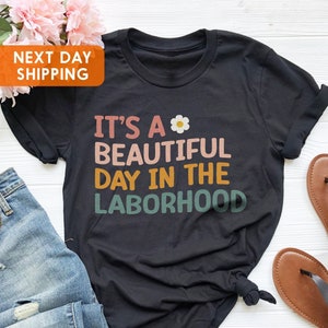 May include: Black t-shirt with a colorful graphic that says "It's a beautiful day in the laborhood" with a small white flower graphic.