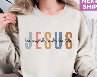 May include: A beige sweatshirt with the words "JESUS the way the truth the life" printed in colorful letters.