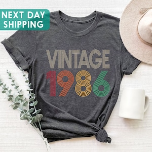 May include: A dark gray t-shirt with the text "Vintage 1986" in colorful retro-style font.