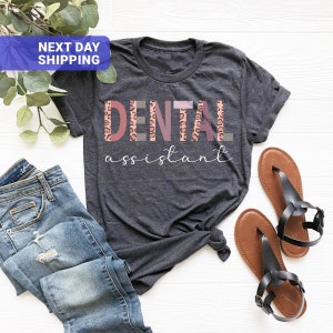Peut inclure: Un t-shirt gris fonc&eacute; avec le texte "DENTAL assistant" en lettres roses, brunes et grises avec un motif l&eacute;opard.