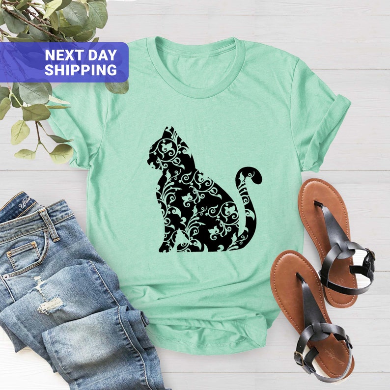 Puede incluir: Una camiseta verde claro con una silueta negra de un gato. El gato est&aacute; hecho de un patr&oacute;n floral.