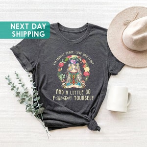 May include: A dark grey t-shirt with a graphic of a woman meditating with flowers and the text "I'm mostly peace, love and light and a little go f yourself".