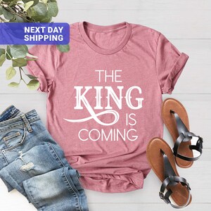 May include: A pink t-shirt with the text "The King is Coming" in white lettering.