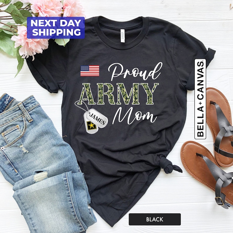 May include: Black t-shirt with a camouflage print "Proud Army Mom" design and a small American flag. The shirt also features a silver dog tag with the name "James" printed on it.