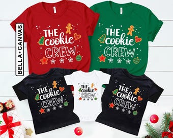 May include: A collection of red, green, black, and white shirts and a baby bodysuit featuring the text THE cookie CREW. The graphic includes illustrations of a gingerbread person, a Christmas tree, a heart, and ornaments with white dots.