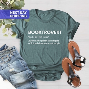 May include: A dark teal short-sleeve t-shirt featuring the white text BOOKTROVERT, the phonetic pronunciation Book-tro-vert-noun, and the definition A person who prefers the company of fictional characters to real people.