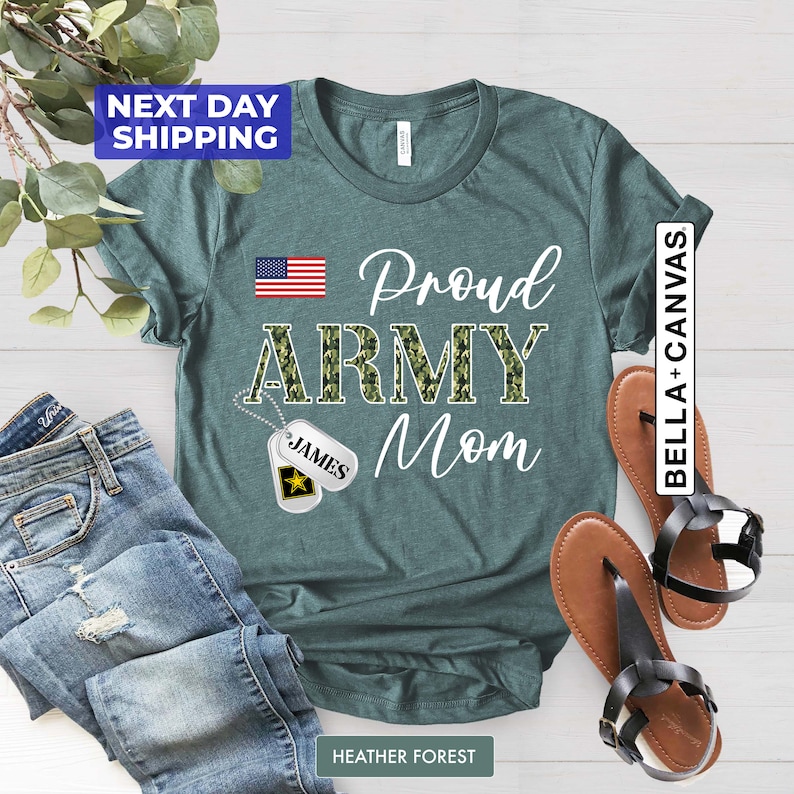 May include: Teal t-shirt with the text "Proud Army Mom" in white. The word "Army" is in camouflage print. A small American flag is in the top left corner. A silver dog tag with the name "James" is hanging from a chain.