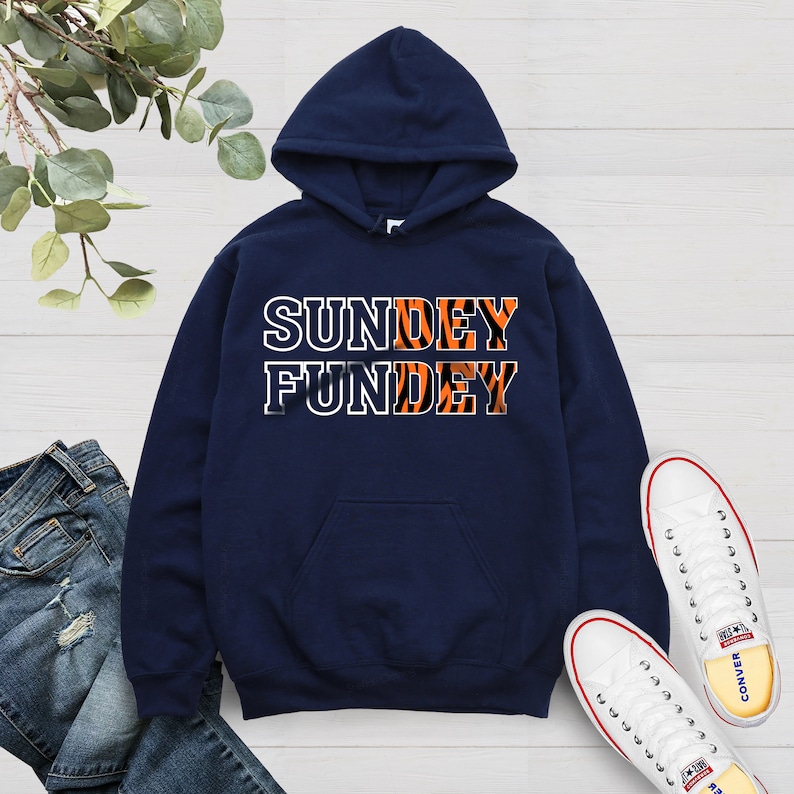 May include: A navy blue hoodie with a white pocket and the text "SUNDEY FUNDEY" in white letters with an orange and black tiger stripe pattern.