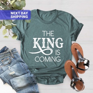 May include: Teal blue t-shirt with white text that reads "The King is Coming".