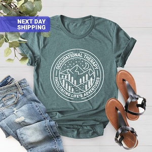 Op de afbeelding: Turquoise T-shirt met een witte afbeelding van een bergketen en de tekst "Occupational Therapy Facilitating Life's Adventures".