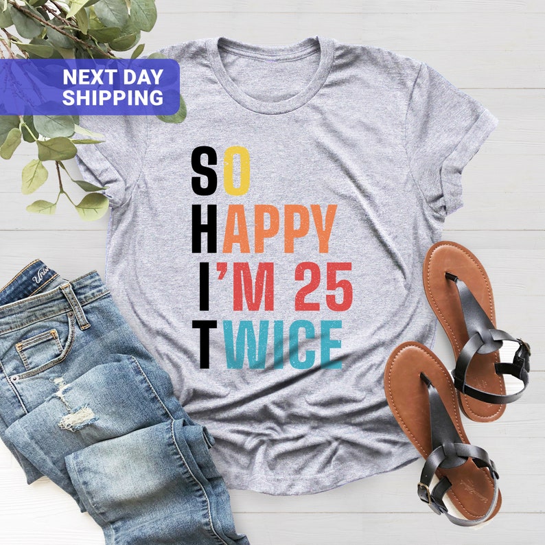 May include: Gray t-shirt with the text "SO HAPPY I'M 25 TWICE" in colorful letters. The letters are stacked vertically.