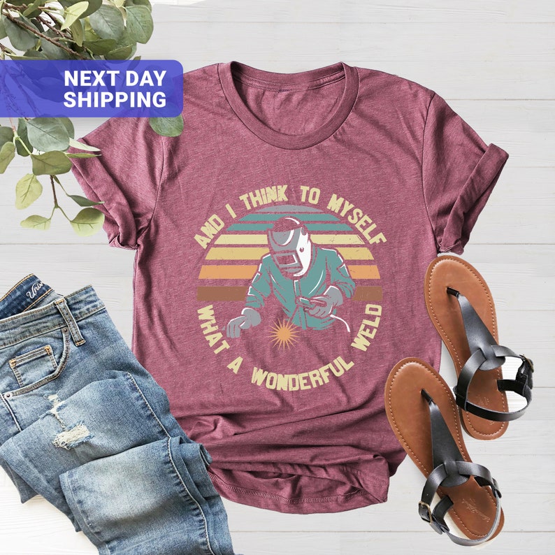 May include: A maroon t-shirt with a vintage-style graphic of a welder with the text "And I think to myself what a wonderful weld".