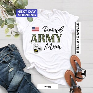 May include: White t-shirt with a camouflage print "Proud Army Mom" design. The shirt also features a small American flag and a dog tag with the name "James" on it.