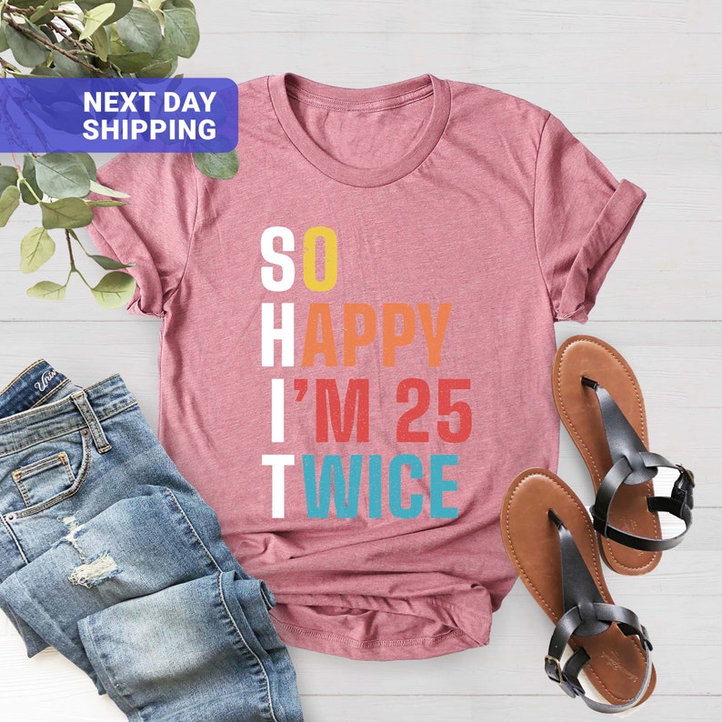 May include: A pink t-shirt with the text "SO HAPPY I'M 25 TWICE" in rainbow colors. The text is in a vertical column with each letter in a different color.