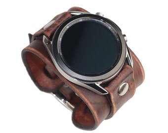 May include: A brown leather watch cuff with a silver watch face. The cuff is made of distressed leather and features a snap closure. The watch face has a black screen and a silver bezel. A stylish accessory.