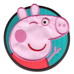 Könnte beinhalten: Gestickter Aufnäher mit einem zwinkernden rosa Schwein mit rotem Oberteil, vor einem türkisfarbenen Hintergrund in einem schwarzen Kreis. Das Schwein hat eine große rosa Wange und zeigt das Friedenszeichen.