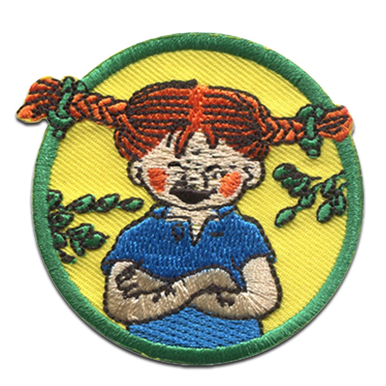 Puede incluir: Un parche redondo bordado con una ni&ntilde;a de dibujos animados con el pelo rojo en trenzas, que lleva una camisa azul y una expresi&oacute;n traviesa. El parche est&aacute; rodeado por un borde verde y un fondo amarillo con hojas verdes.