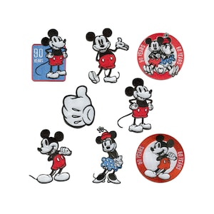 Peut inclure: Neuf patchs brodés représentant Mickey Mouse dans différentes poses et designs. Certains patchs incluent le texte "90 Years" et présentent Mickey Mouse avec Minnie Mouse. Les patchs sont tous rouges, blancs et noirs.