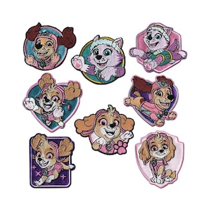 May include: A collection of embroidered patches featuring characters from the animated series, Paw Patrol. The patches showcase Skye and other characters in various poses, with pink, purple, and blue color schemes. Each patch has a detailed design.