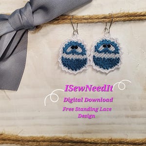May include: A pair of blue and white free-standing lace earrings with a cute face design. The earrings are hanging from silver hooks. The text "ISewNeedIt Digital Download Free Standing Lace Design" is visible below the earrings.