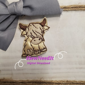 May include: Embroidered design of a brown and white Highland cow with a fluffy mane, sitting on a white wooden surface. The design is surrounded by a gray bow and brown twine. The text "iSewNeedIt Digital Download" is visible below the design.