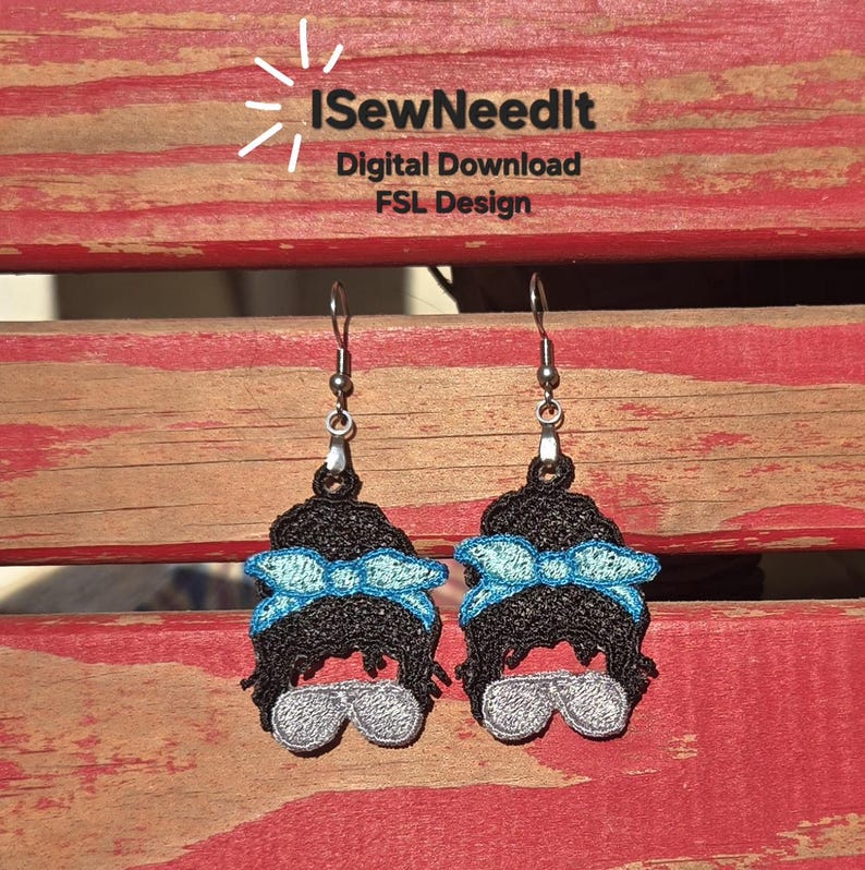 May include: A pair of handmade earrings depicting a black hair bun with a light blue bow and silver sunglasses. The earrings are displayed on a red and brown wooden surface. The text "I SewNeedIt" is visible.