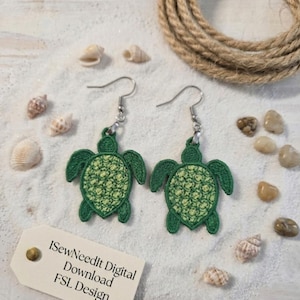May include: A pair of green turtle-shaped earrings with a textured design, displayed on a sandy surface with seashells and a rope. The earrings have silver-colored hooks. A tag reads "ISewNeedIt Digital Download FSL Design."
