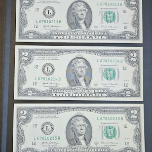 May include: Three United States two-dollar bills. Each bill features a portrait of Thomas Jefferson and the text "Two Dollars." The bills are green and black with intricate border designs and serial numbers. The bills are arranged in a vertical stack.