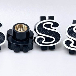 May include: Four black tire valve stem caps with a white dollar sign design. Each cap has a threaded brass insert for attaching to a tire valve.