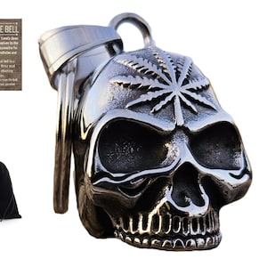 May include: A silver-colored motorcycle ride bell shaped like a skull with a cannabis leaf design on top. Includes a small metal ring, a mounting bracket, and a black drawstring bag. A wooden sign with text is also included.