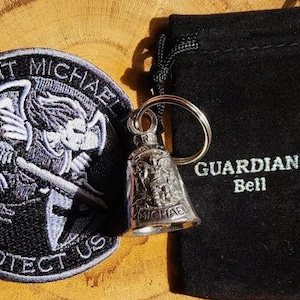 May include: A silver keychain bell with a Saint Michael design and the words "GUARDIAN® Bell" on a black velvet pouch. The bell is attached to a silver key ring.