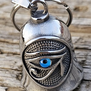 May include: Silver motorcycle bell with a blue evil eye design. The bell has a ring attached to the top.