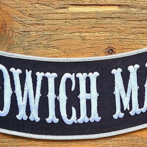 May include: A black and white embroidered patch with the text "SANDWICH MAKER" in white lettering.