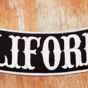 May include: Black and white motorcycle patch with the word "CALIFORNIA" in a white, stylized font.