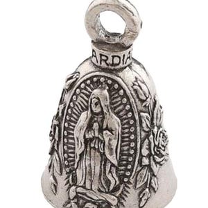 May include: Silver-colored bell with a loop at the top and the word "ARDIA" above a central image of a religious figure. The bell is decorated with floral and religious motifs, and is likely a motorcycle or vehicle accessory.