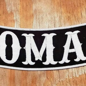 May include: Black and white embroidered patch with the word "NOMAD" in white lettering on a black background.