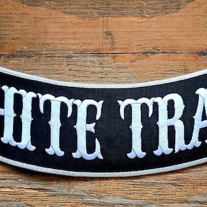 May include: White on black embroidered patch with the text "WHITE TRASH" on a curved background.